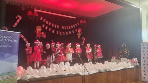 Dzieci na scenie w strojach mikołajkowych śpiewające piosenki